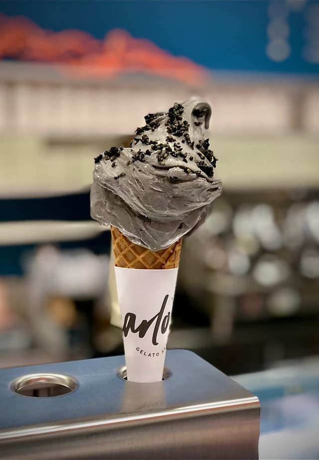 Black sesame gelato in a waffle cone standing on the shop counter