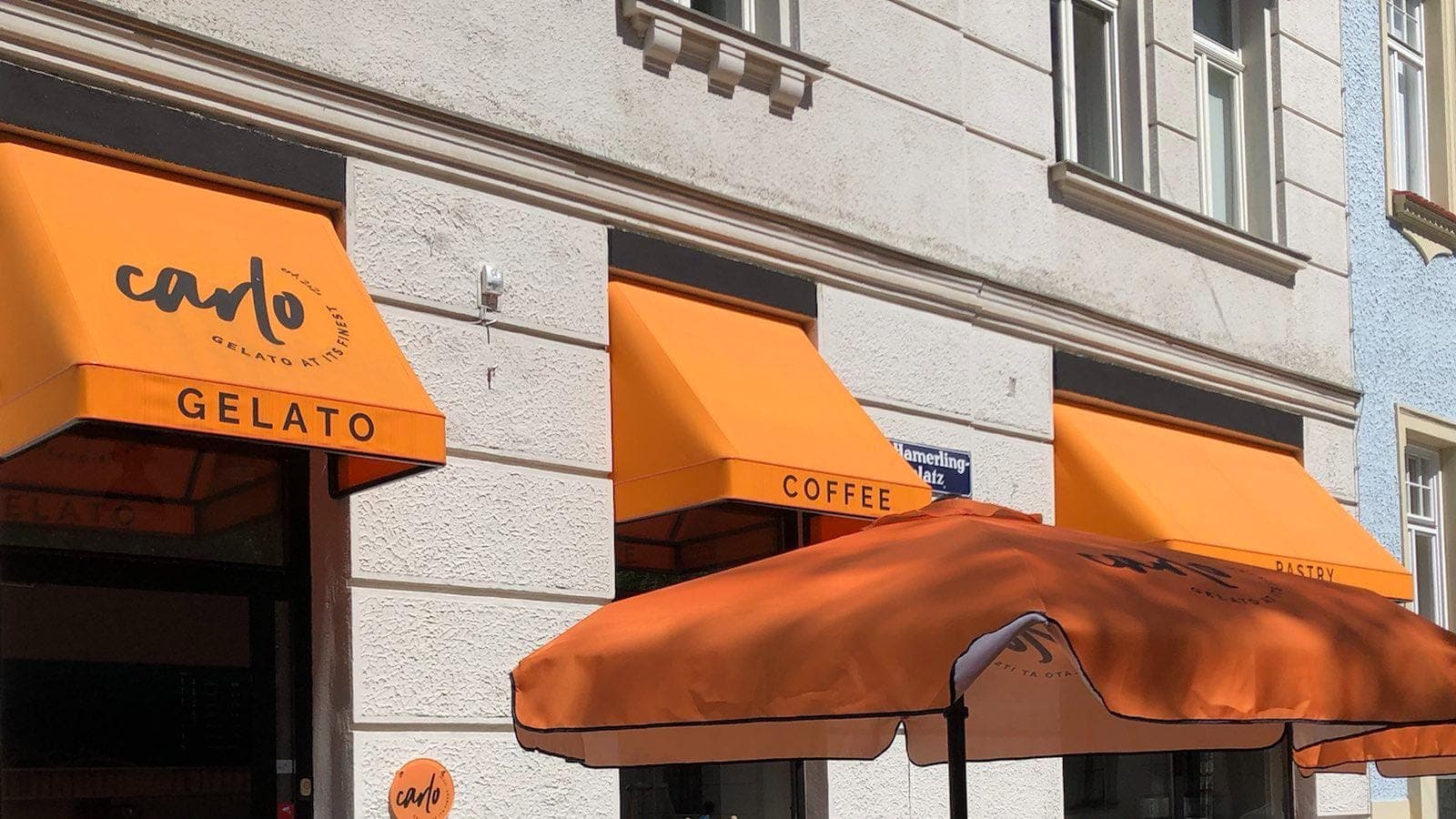 Gelato shop front with orange carlo awnings and a matching parasol on the pavement